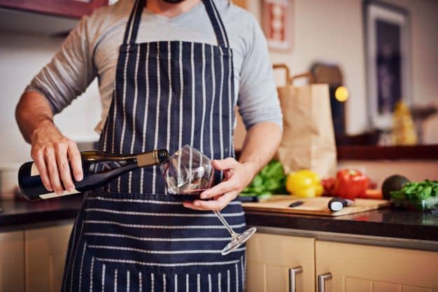 Man die een glas wijn inschenkt tijdens het koken